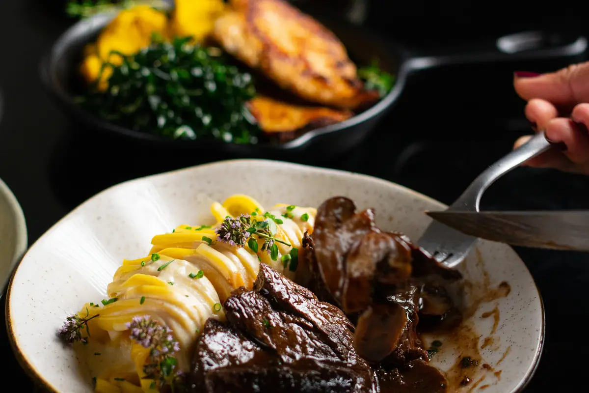 Carne assada ao molho com purê, servida em tigela clara sobre fundo escuro